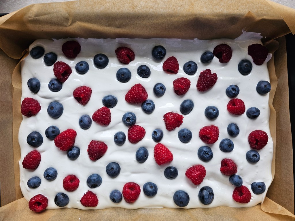 A tray with baked shortbread cake base, a layer of meringue, blueberries and raspberries on top - before baking