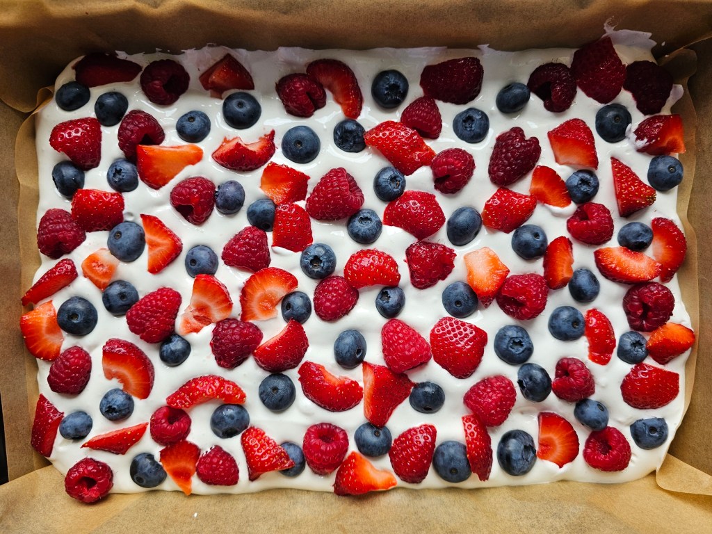 A tray with baked shortbread cake base, a layer of meringue, and berries on top - before baking