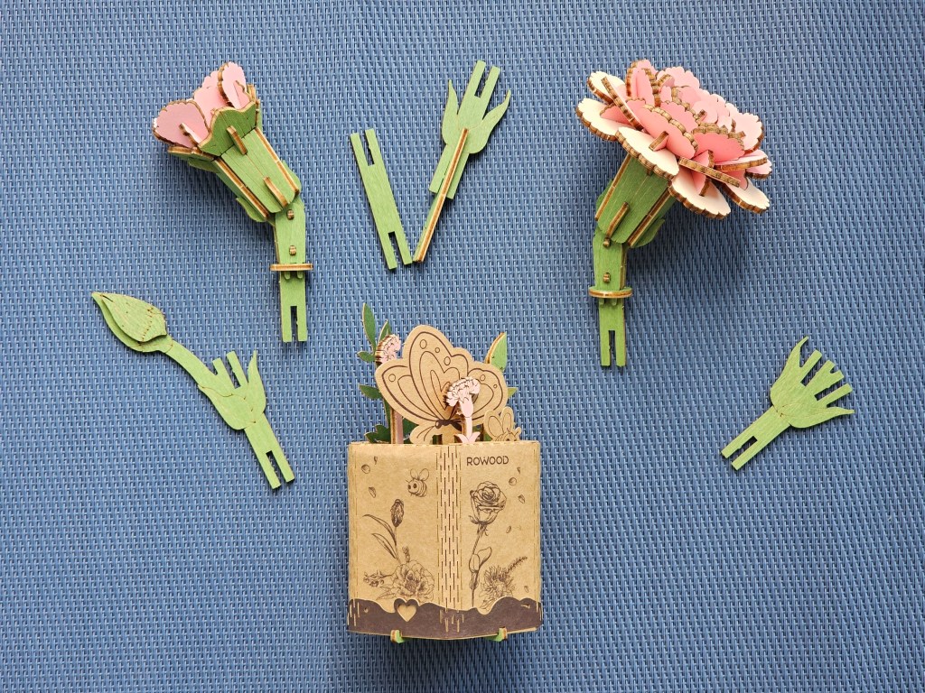 Assembled individual parts of wooden pink carnations: there are stems, a large flower, a small flower, and a pot/stand