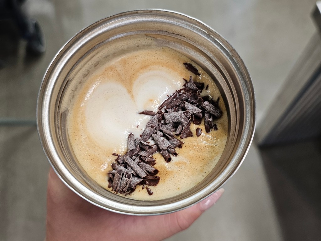 A metal travel mug with a cappuccino and flakes of real chocolate