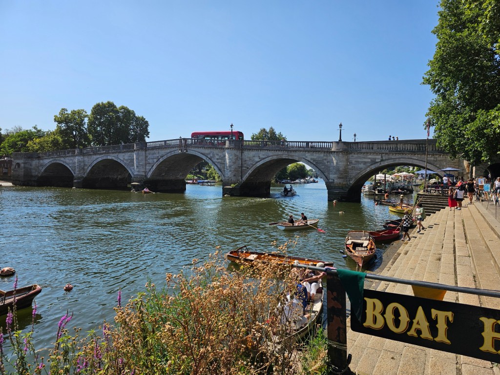 A bridge over the Thames in Richmond. There's a red bus on the bridge. The sky is blue with no clouds.