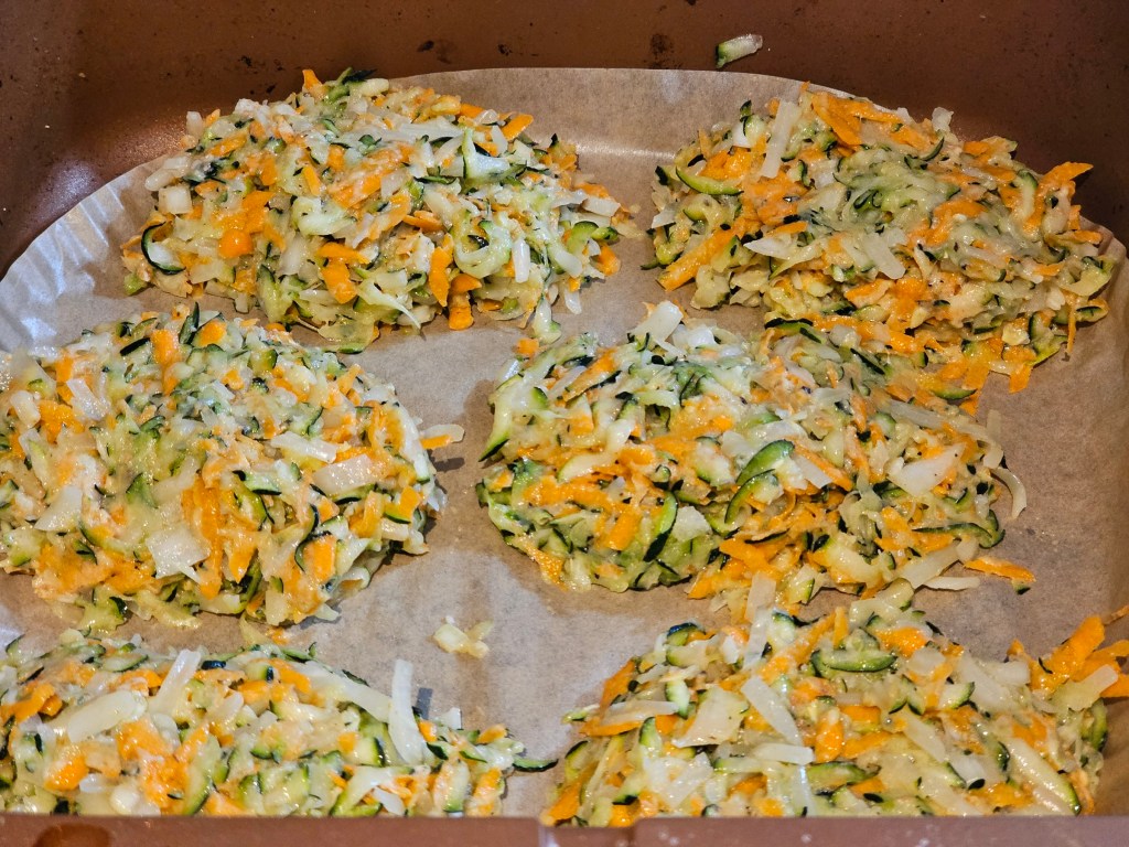 Shaped courgette and carrot fritters lined in an air fryer, before baking