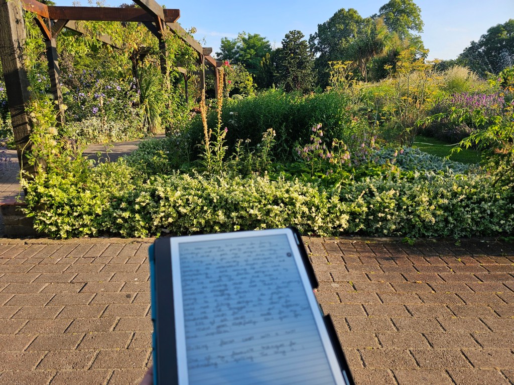Writing on Kindle Scribe in a park - there are flowers seen and blue skies