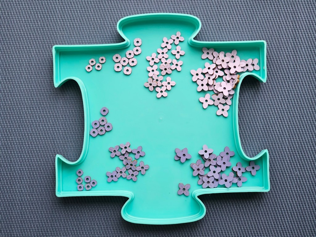 A few dozen tiny wooden flowers in four sizes, in purple and pink, on a teal tray.