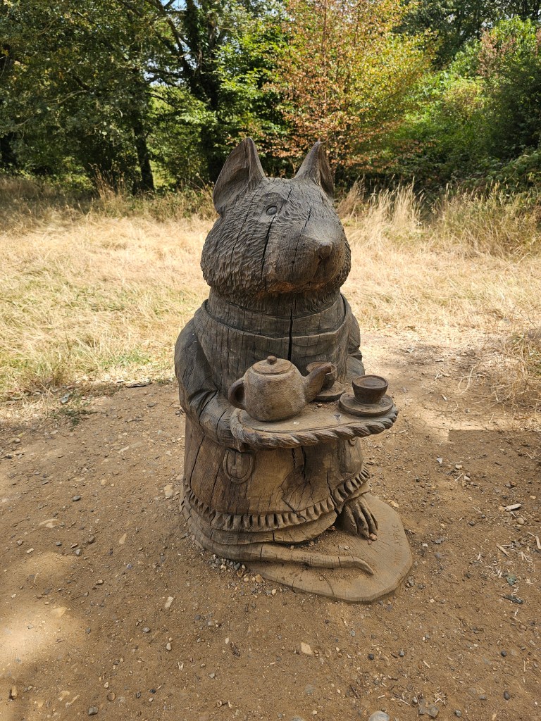 A wooden sculpture depicting a rodent holding a tray with a teapot and a teacup