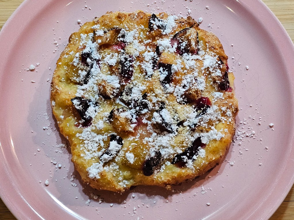 Baked high protein plum pastry, on a plate, sprinkled with icing sugar.