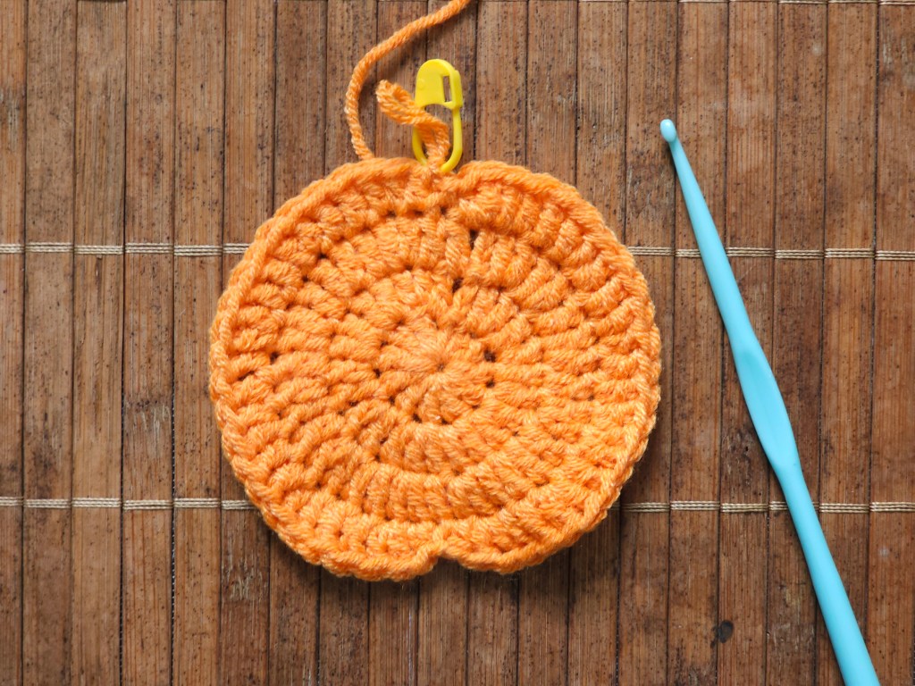 Half-finished crocheted pumpkin coaster. After a few rounds of treble crochets, the coaster is starting to resemble a pumpkin
