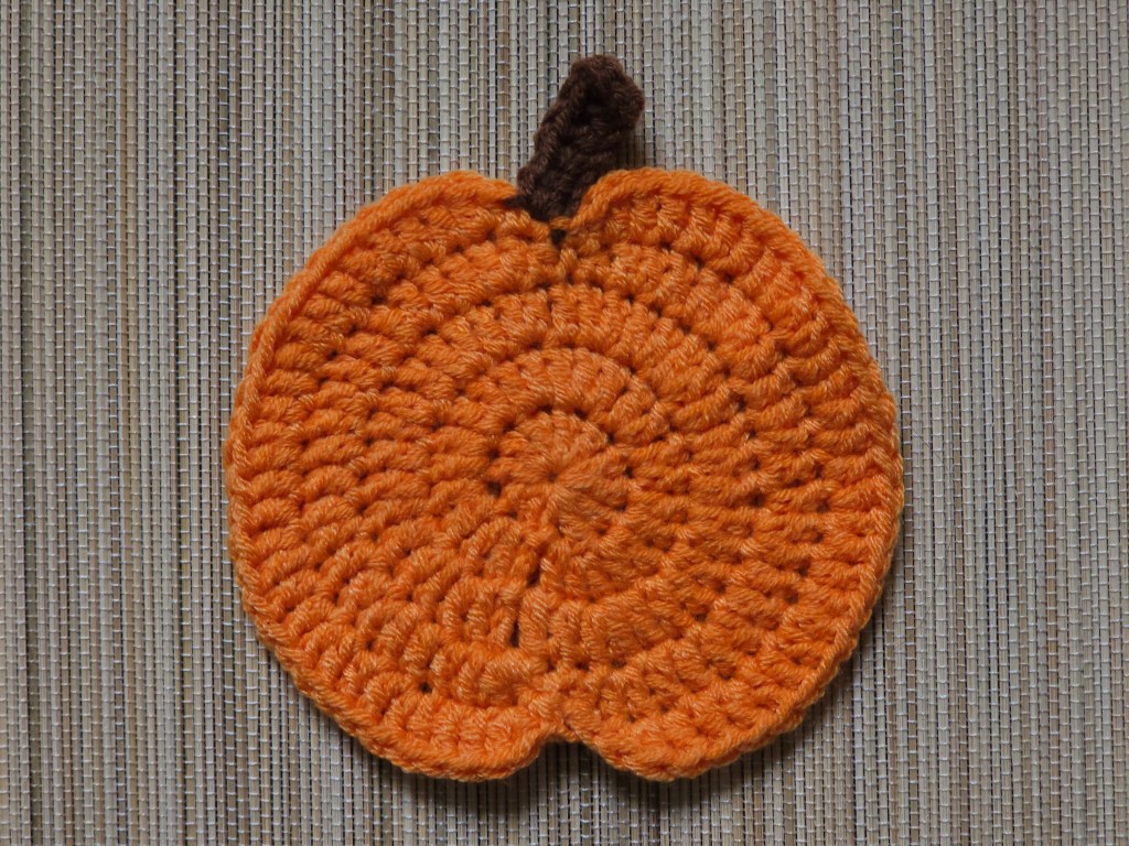 Completed orange crocheted pumpkin coaster with a brown stem