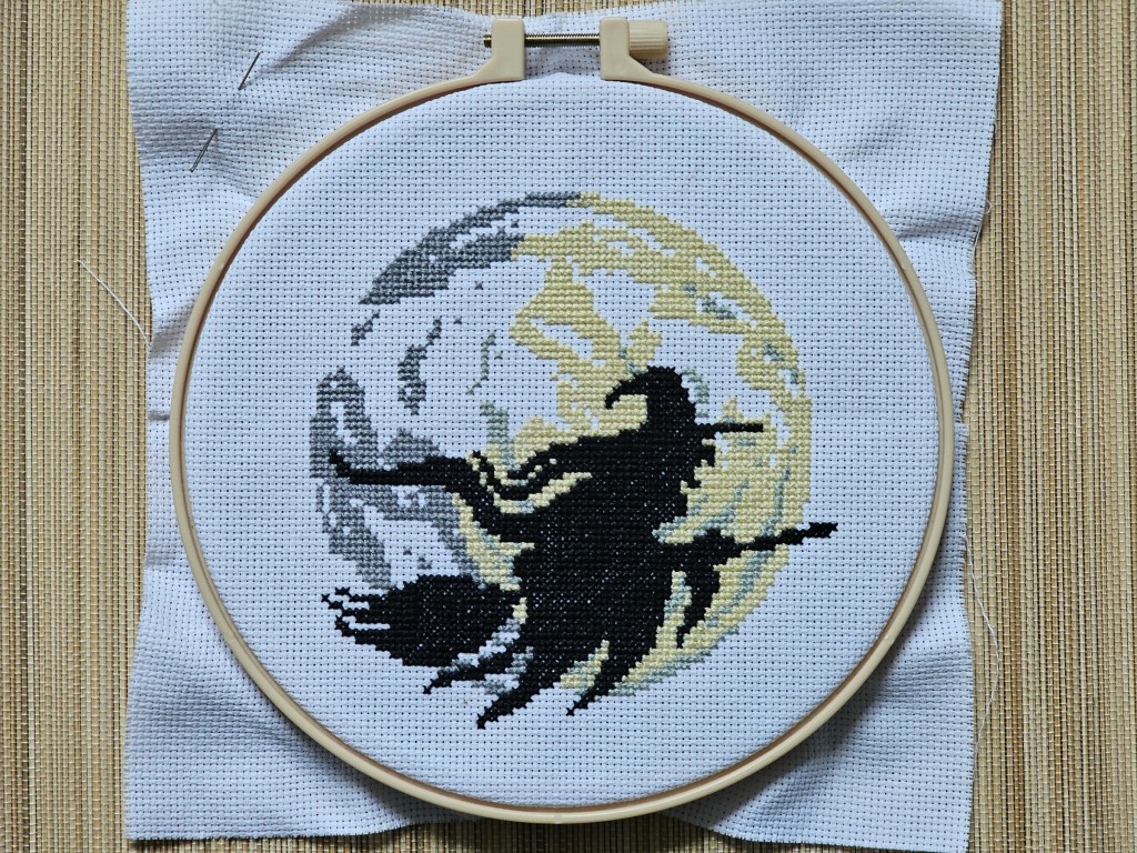 Nearly finished cross stitch project depicting a witch on a flying broom in front of a large moon