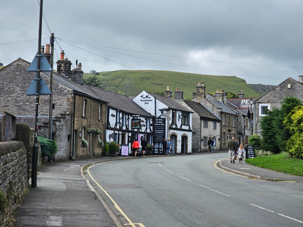 The old stone houses in Castleton, Peak District. Some hills can be seen in the background. There are heavy rain clouds above the town.