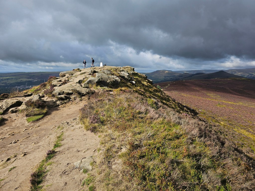 The top of Winn Hill in Peak District, with interesting rock formations and the trig point. Other hills can be seen all around.